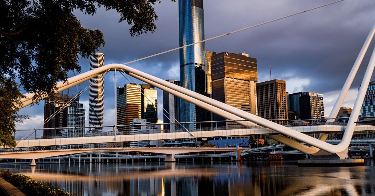 A striking view of a modern bridge and city skyline over Brisbane River at sunrise.